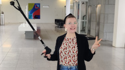 Nainen roskapihdit kädessä, taustalla kaupungintalon aula.