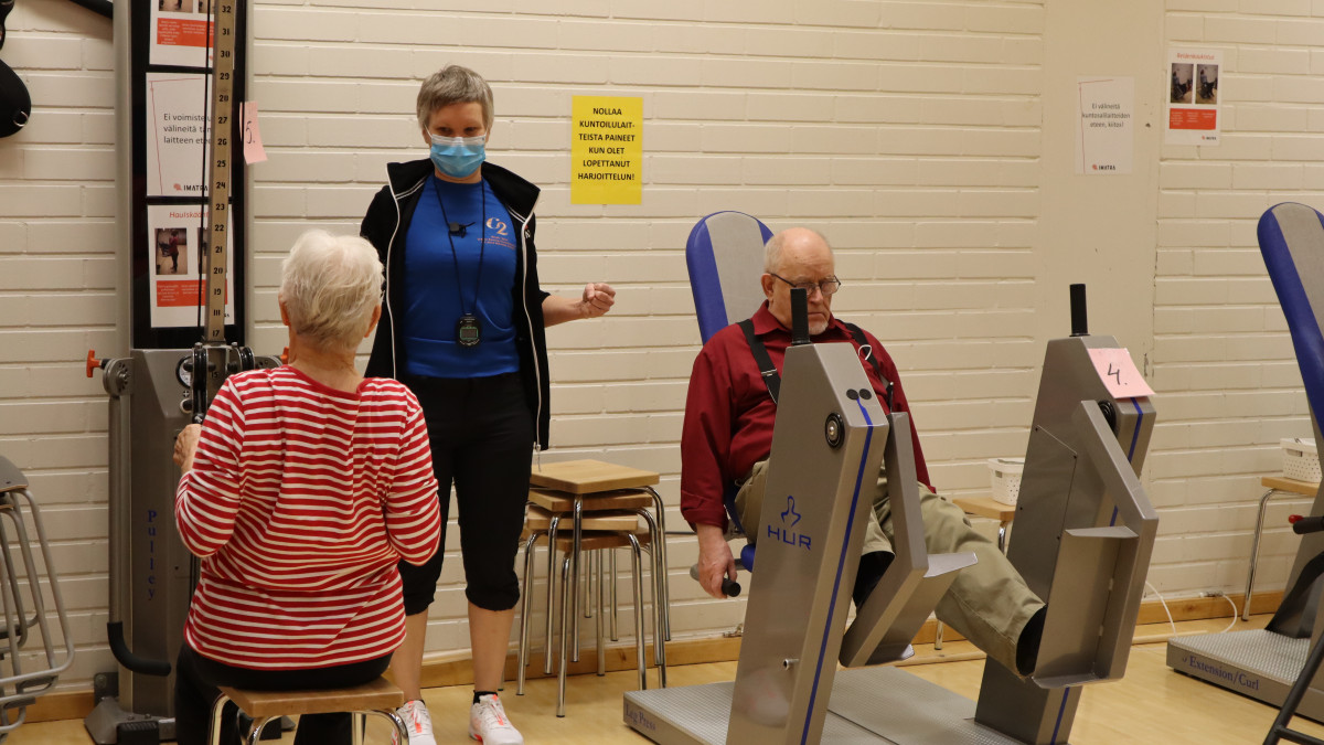 Liikunnanohjaaja iäkkäiden ryhmässä kuntosalilaitteiden kanssa.