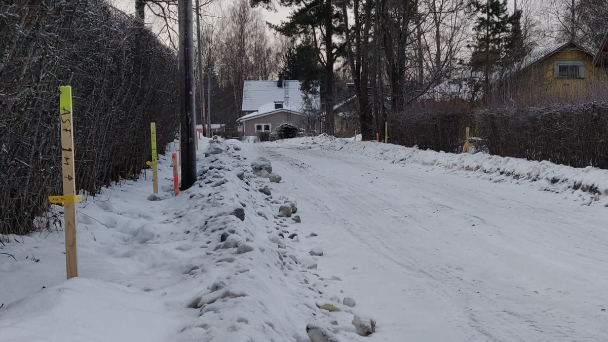 Talvinen näkymä kadulta, jonka reunoilla pensasaitaa ja pari omakotitaloa.