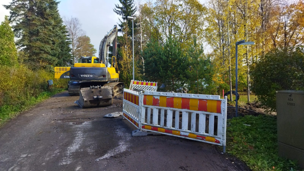 Kaivinkone ja työmaan aitaa kapealla kadulla.