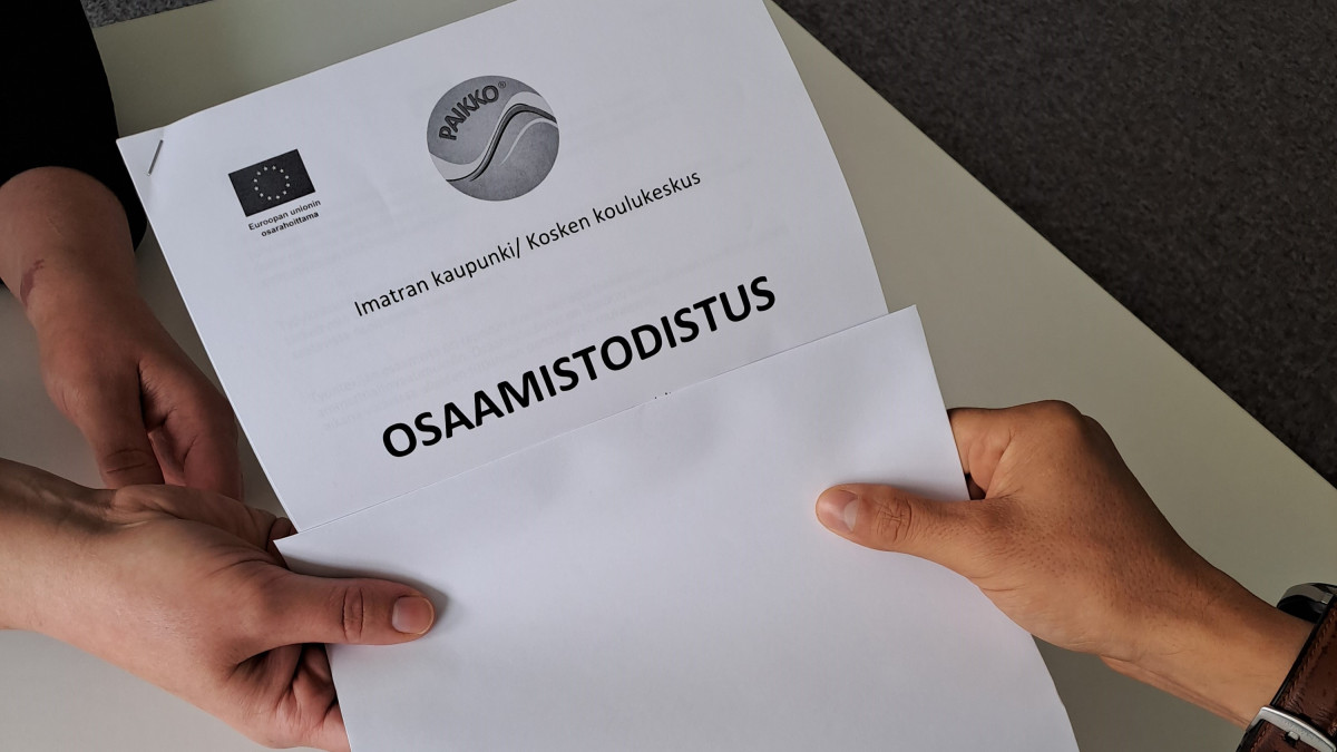 Kaksi kättä pitää kiinni osaamistodistuksesta.