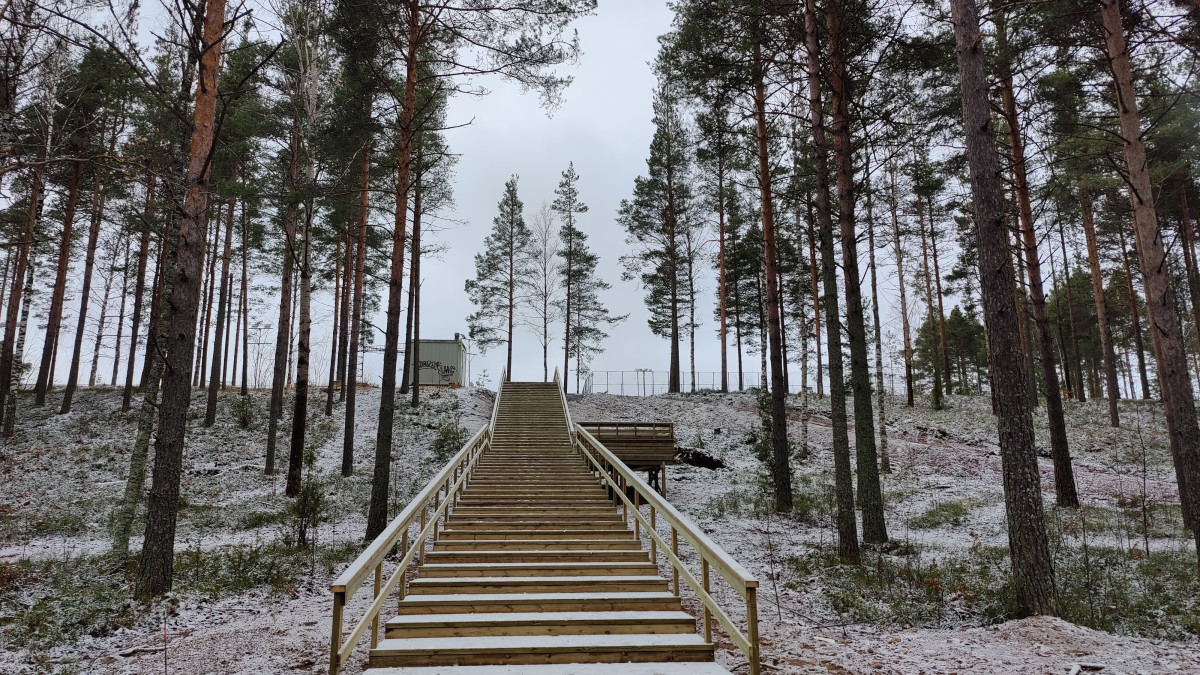 Kuntoportaat nousevat rinteellä, jossa ohut lumikerros harmaana päivänä.