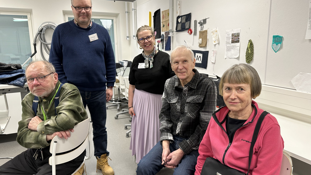 Viisi henkilöä hymyilee kameralle asukasillassa Vuoksenniskan koulun luokassa.