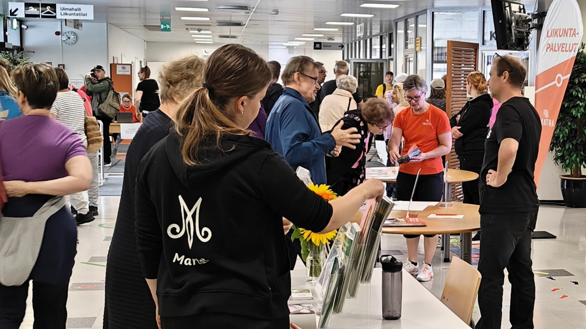 Urheilutalon aulassa tapahtuman yleisöä ja esittelijöitä.