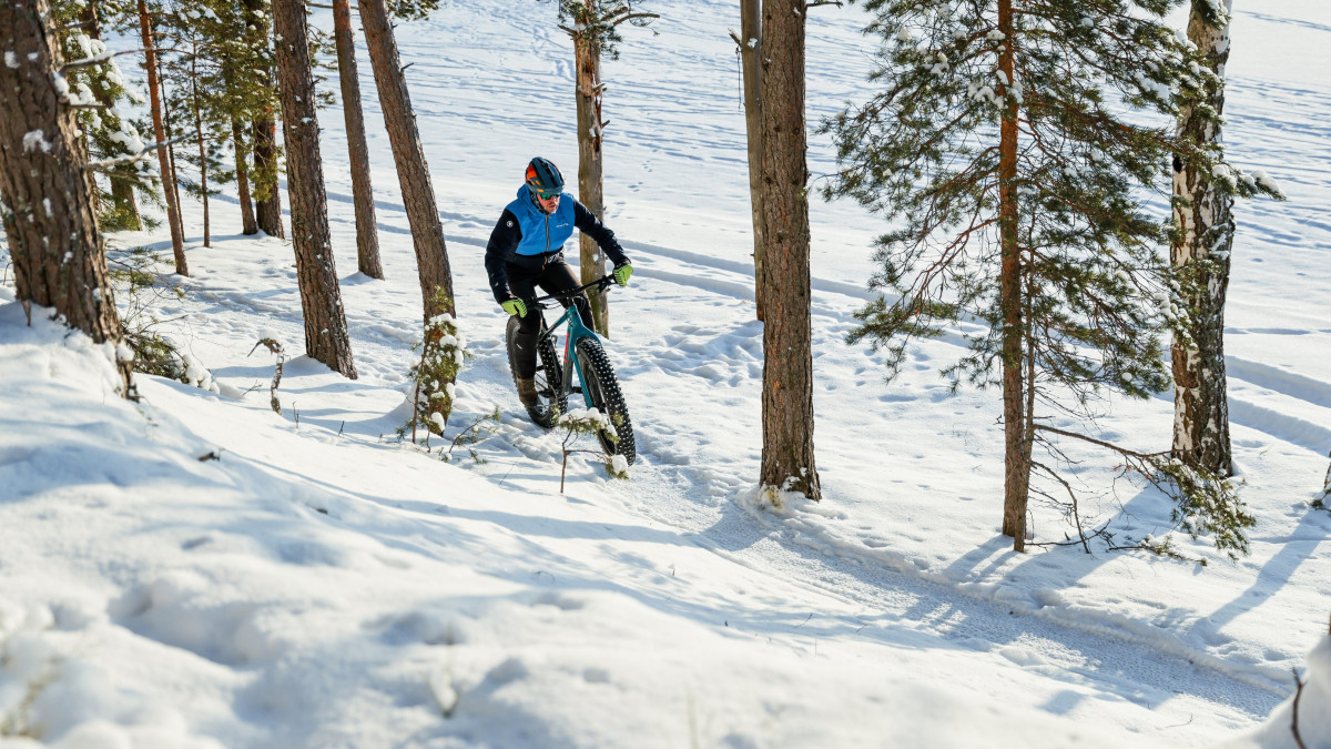 Maastopyöräilijä aurinkoisessa talvisäässä metsäpolulla.