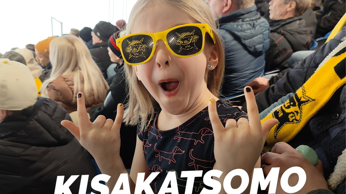 Lapsi täydessä jääkiekkokatsomossa keltasankaiset aurinkolasit päässä.