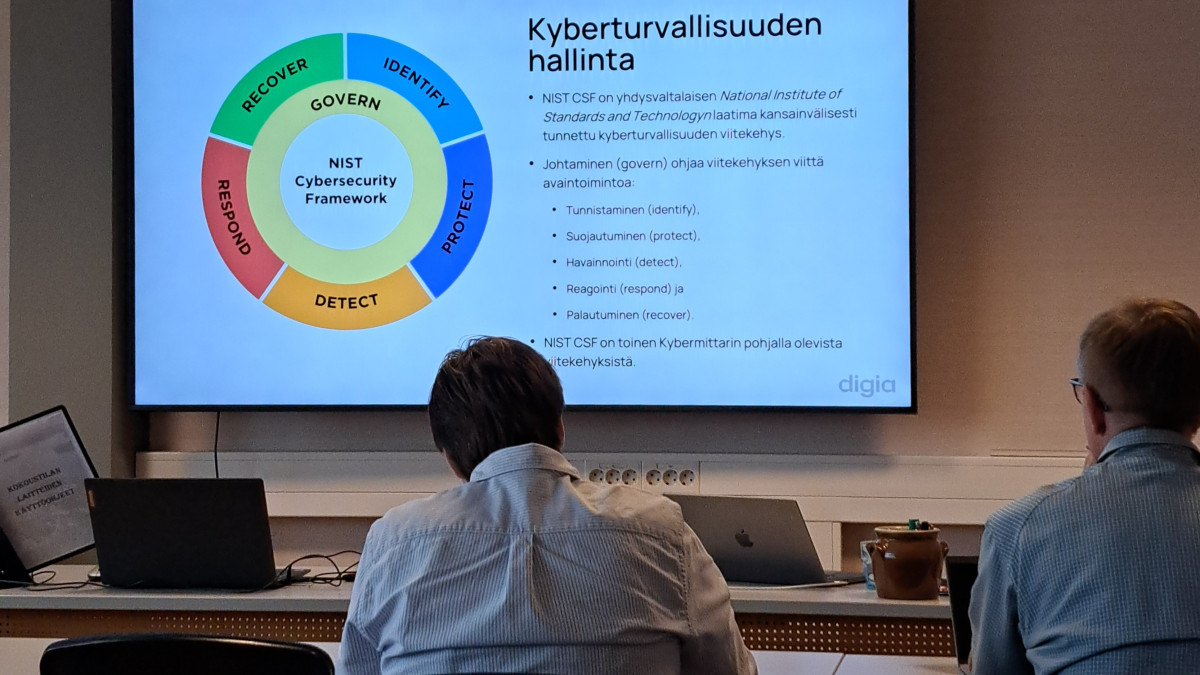 Kaksi miestä katsomassa diaa, jonka otsikko on "Kyberturvallisuuden hallinta".