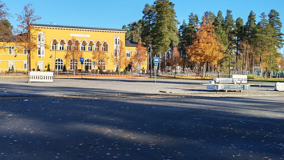 Parkkialue, jonka takana näkyy keltainen kouluraknneus.