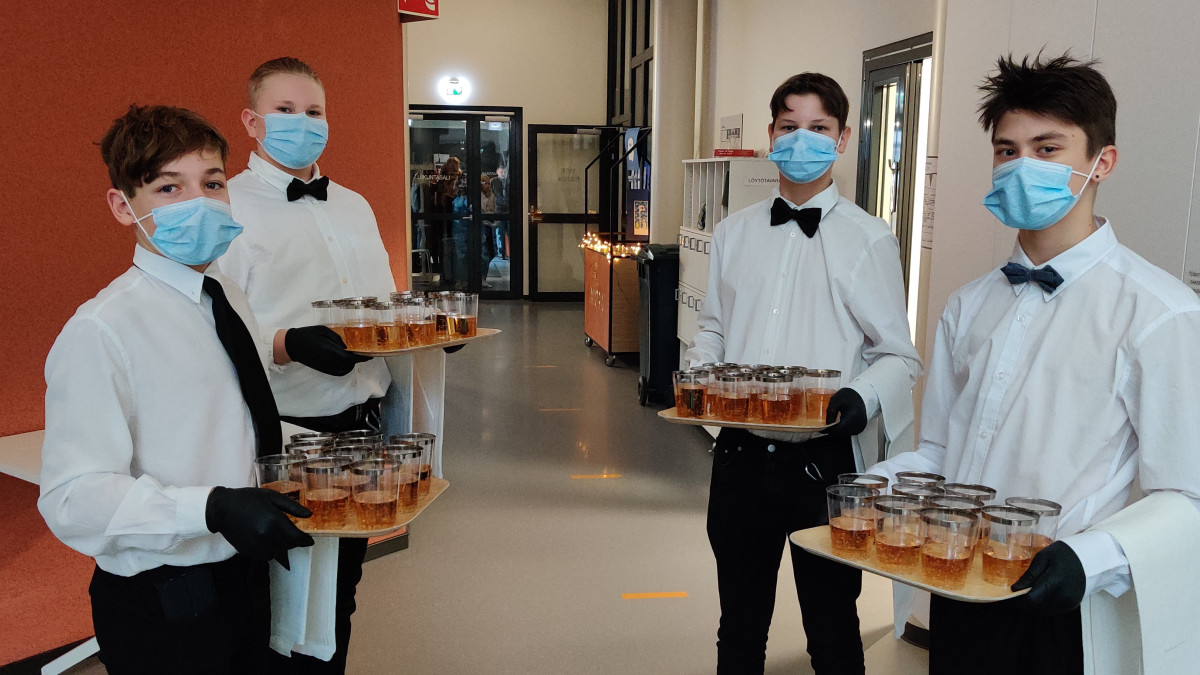 Neljä nuorta tarjoilijapoikaa maljatarjottimien kanssa.