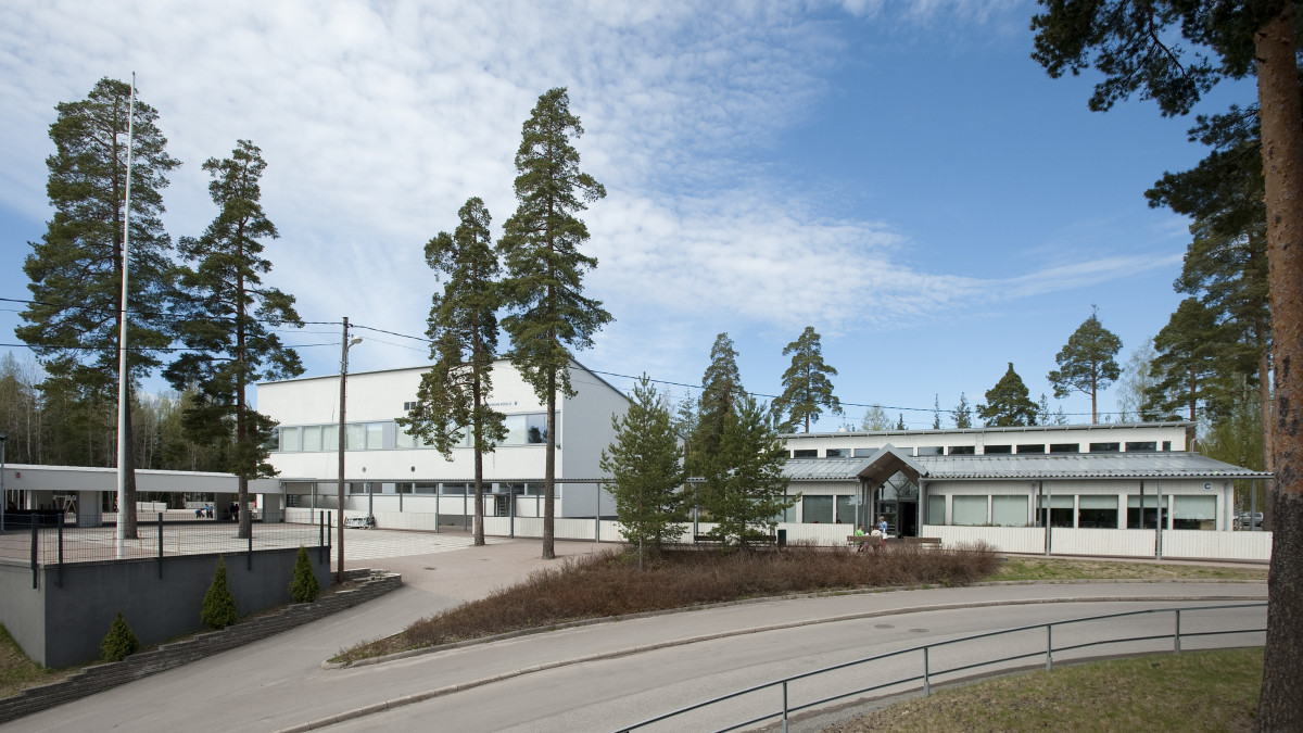 Valkoinen koulurakennus, ympärillä mäntyjä.
