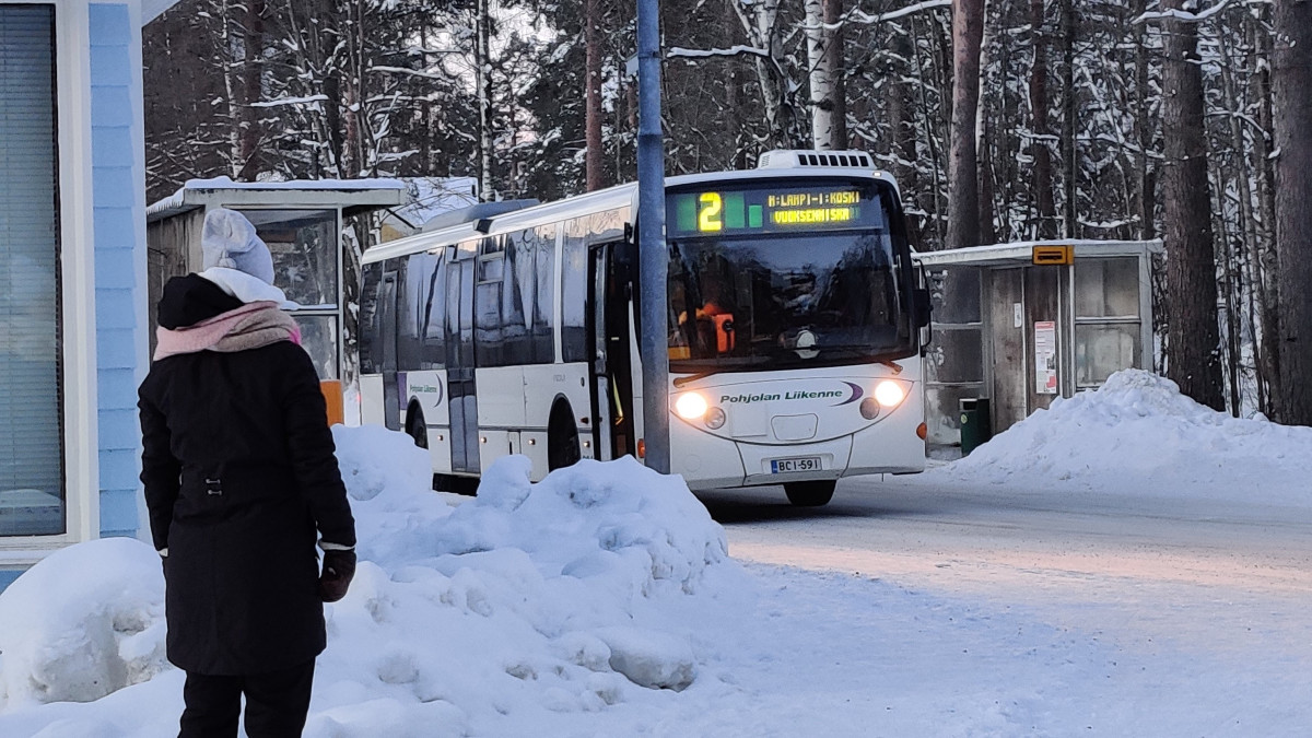 Bussi pysäkillä ja saattaja seuraa bussin lähtöä.