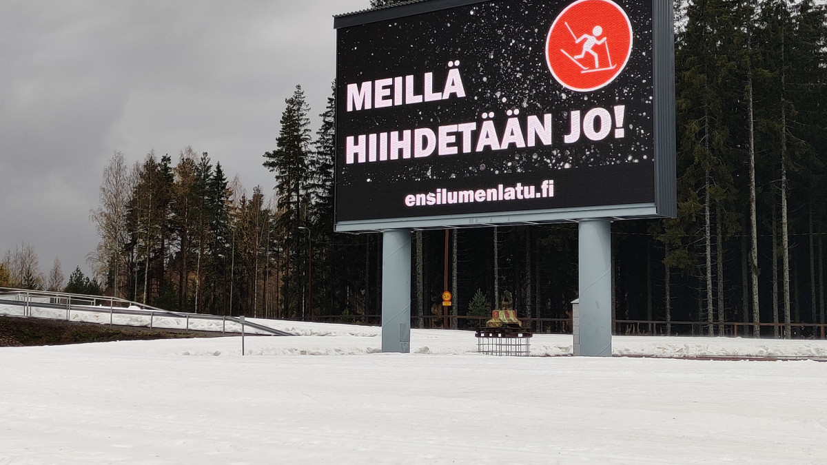 Ensilumenladun kyltti, jossa lukee meillä hiihdetään jo.