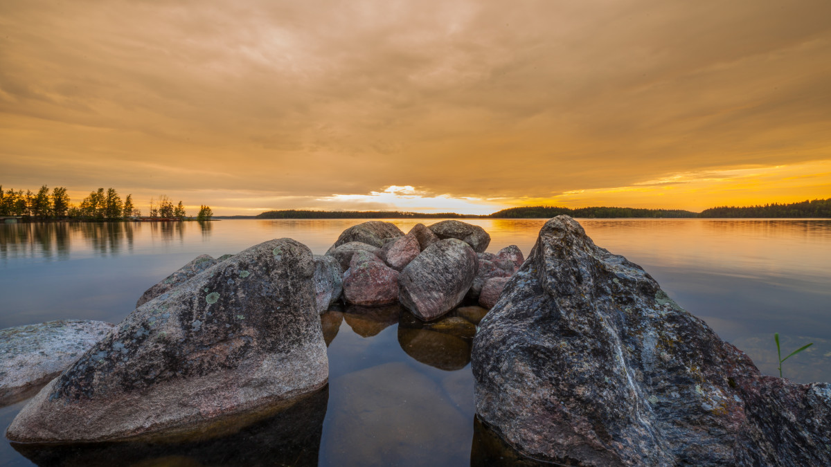 Saimaan ranta illalla auringon laskiessa, etualalla isoja kiviä.