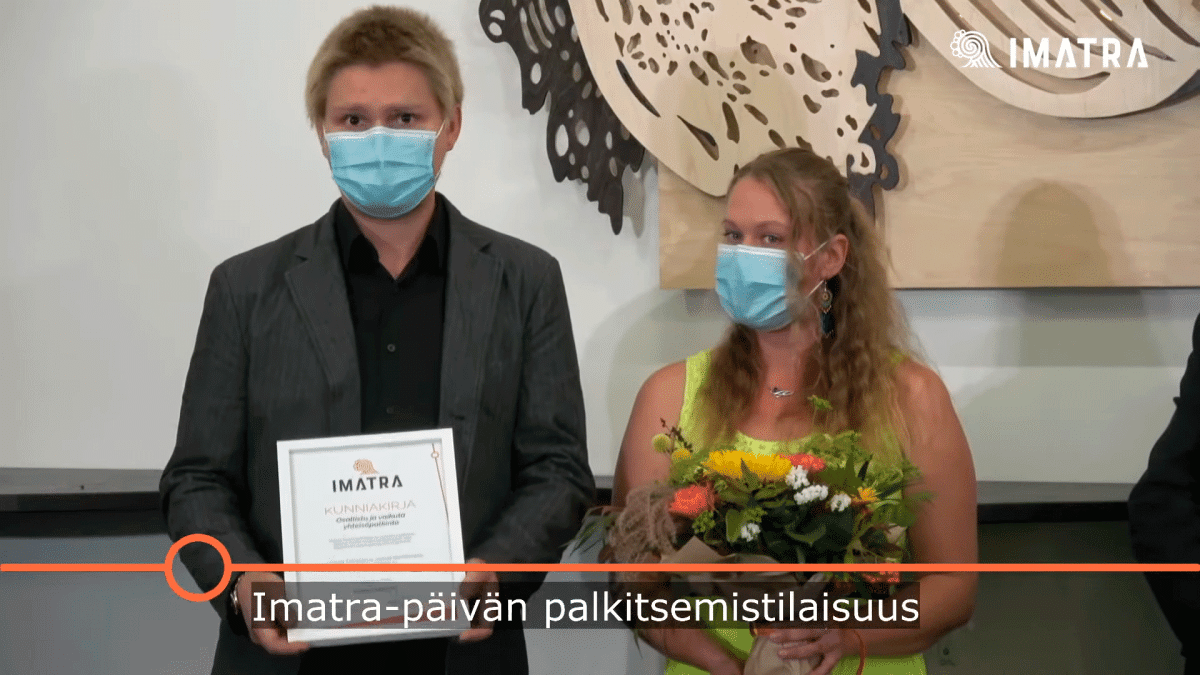 Mies ja nainen maskeissa, kunniakirja ja kukat kädessä.