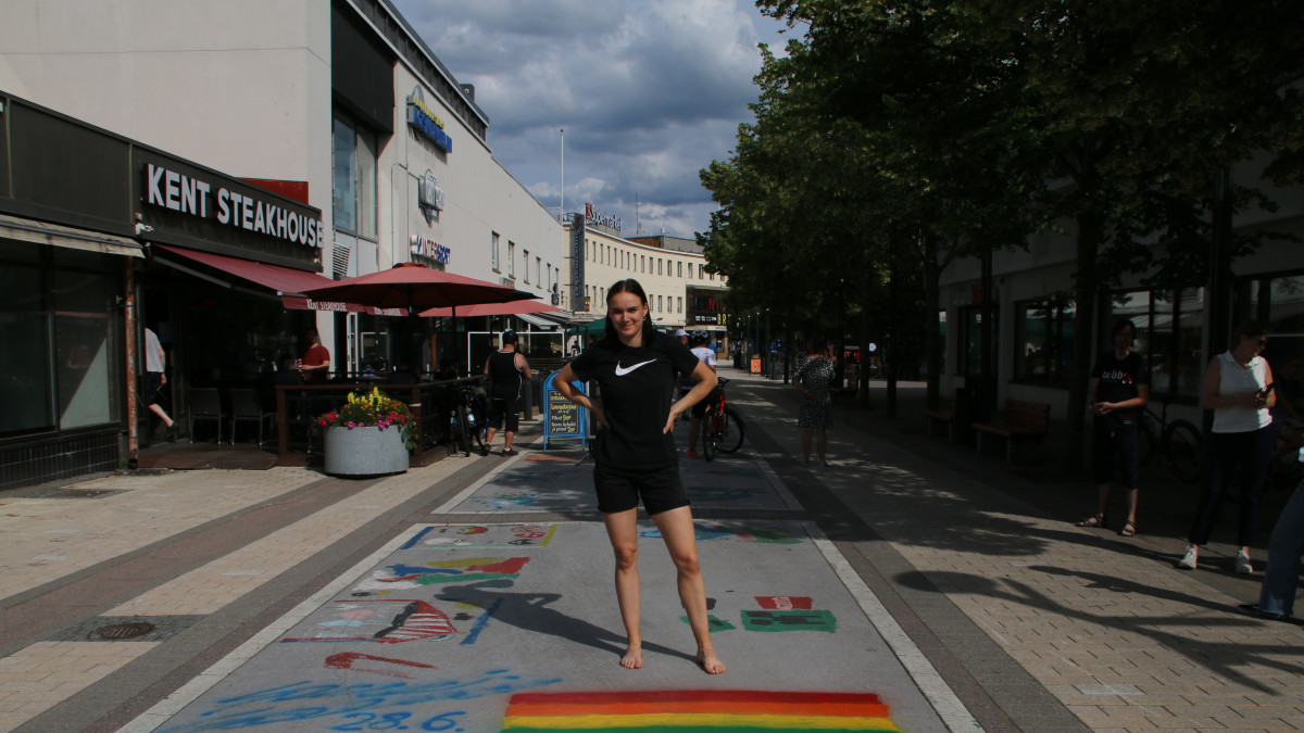 Salminen seisoo maalaamansa pride-lipunn takana, taustalla kävelykatu.