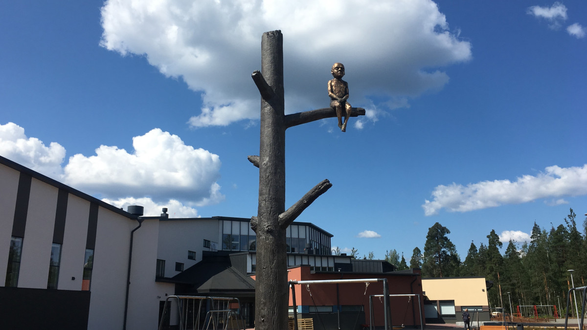 Keskelle koulun pihaa pystytettiin alumiininen kelohonka, jonka oksalla istuu pronssinen poika.