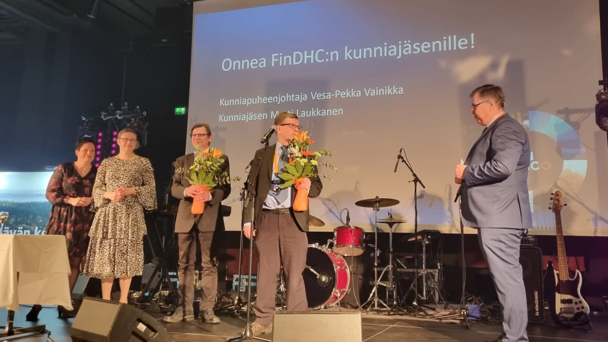 ihmisiä lavalla ja kahdella miehellä kukkapuskat sylissä.