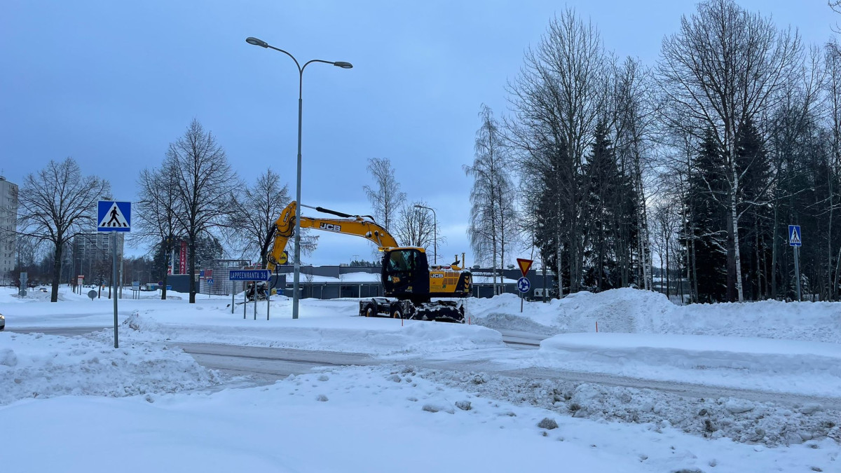 Kaivinkone mataloittaa risteyksen lumivalleja.