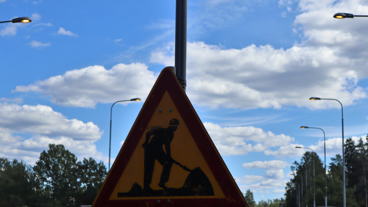 Tietyömerkki, jonka taustalla on taivas ja katuvalaisimia.