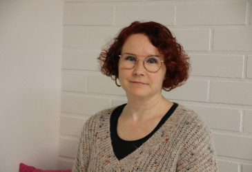 Taina Leskinen istuu ja katsoo kameraan.