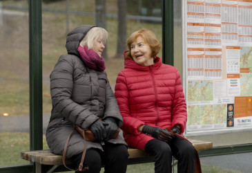 Kaksi vanhaa naista istumassa bussipysäkillä .