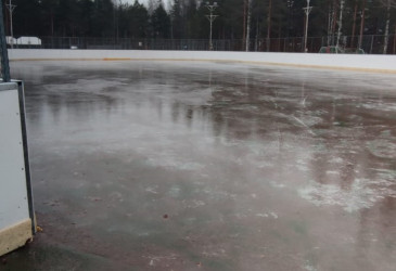 Jäätä hiekkakentän päällä, taustalla kaukalon laita ja männikköä.