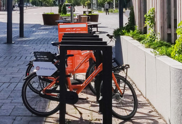 Oranssinväriset kaupunkipyörät kesäisenä päivänä omalla asemallaan.
