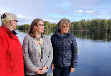 Kolme vanhaa naista seisomassa, taustalla joki.