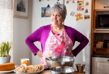 Mummoksi pukeutunut nainen täyden ruokapöydän takana keittiössä.