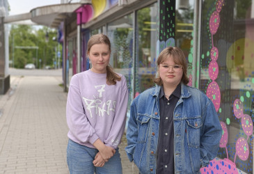Kaksi nuorta seisovat Imatralla värikkään rakennuksen vierellä kävelykadulla.