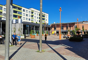 Aukio, jolla kolme ihmistä, pylväitä etualalla.