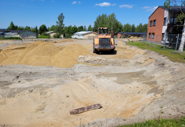 Kaivuri hiekkakentällä asuinrakennusten vieressä.