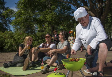 Kokin asuinen mies grillaamassa makkaraa puistoseurueen kanssa.
