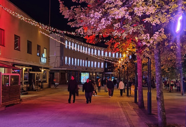 Kävelykatu Koskenparras iltavalaistuksessa punasävyisin valoin, ihmisiä kävelyllä.