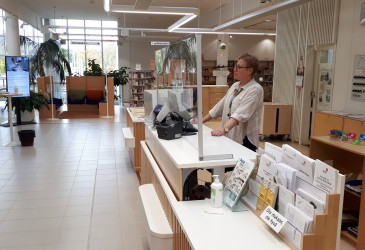 Kirjastovirkailija seisoo Imatran pääkirjaston lainaustiskin takana, kuva sivusta.