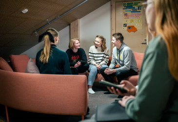 Nuoret istuvat sohvalla ja keskustelevat hymyssä suin.