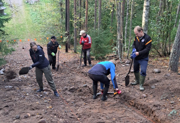 Viisi ihmistä lapioden kanssa kaivamassa sorarinteessä.