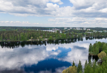 Maisemakuva, jossa etualalla Vuoksen tyyni pinta ja taka-alalla siintävät Mansikkalan tornitalot. 