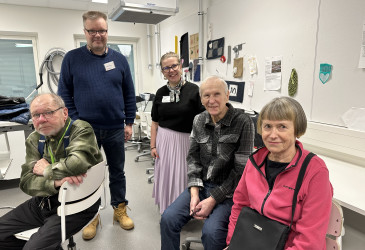 Viisi henkilöä hymyilee kameralle asukasillassa Vuoksenniskan koulun luokassa.