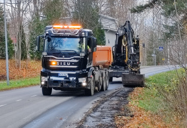Kuorma-auto ja kaivinkone poistamassa tien reunapalteita.