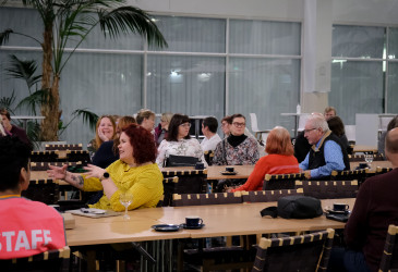 Ihmisiä pöytien ääressä istumassa ja keskustelemassa.