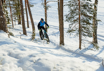 Maastopyöräilijä aurinkoisessa talvisäässä metsäpolulla.