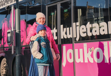 Aikuinen ja lapsi seisovat pinkin bussin vieressä.