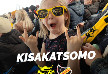 Lapsi täydessä jääkiekkokatsomossa keltasankaiset aurinkolasit päässä.