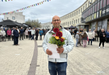 Mies seisoo kävelykadulla kukkakimppu ja kunniakirja käsissään.