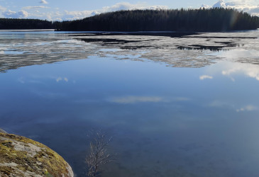 Viimeiset jäät sulamassa tyynen järven pinnasta auringonpaisteessa.