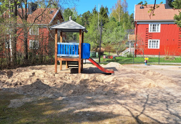 Hiekkakenttä, liukumäki ja vanha puutalo taustalla.
