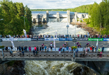 Imatrankoski kuohuu ja sillalla Saimaa Cycle Tour-tapahtuman mainoksia ja yleisöä.