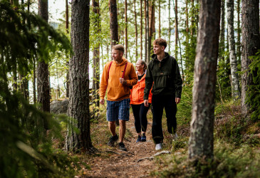 Kolme kävelijää metsäpolulla.