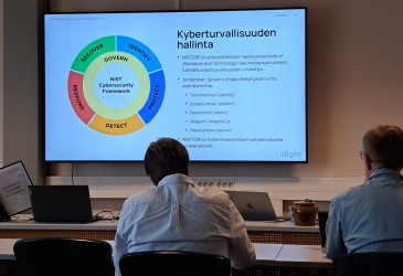 Kaksi miestä katsomassa diaa, jonka otsikko on "Kyberturvallisuuden hallinta".